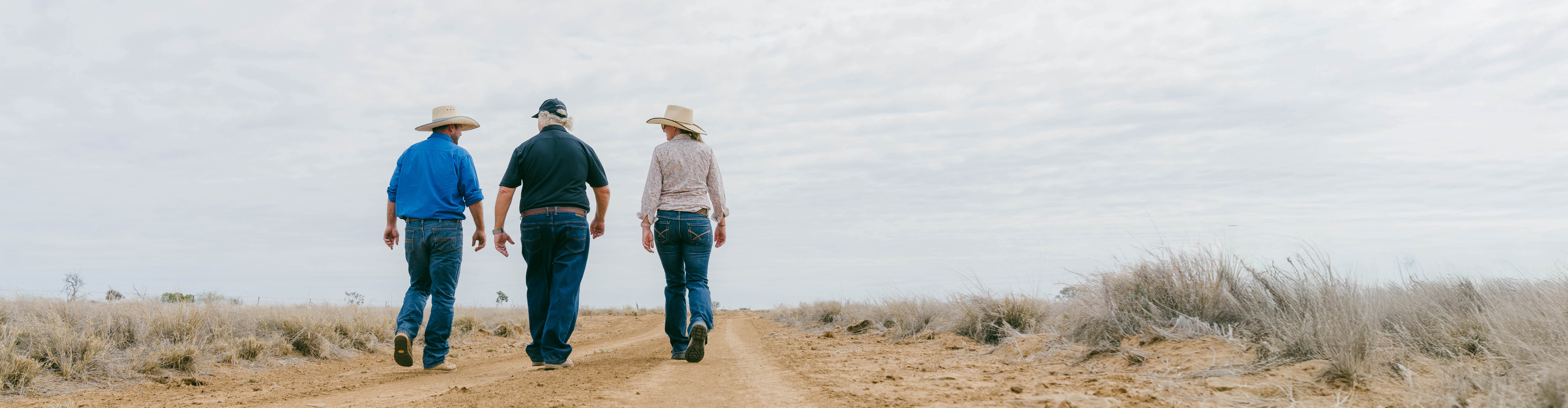 Three people walking up a dusty road